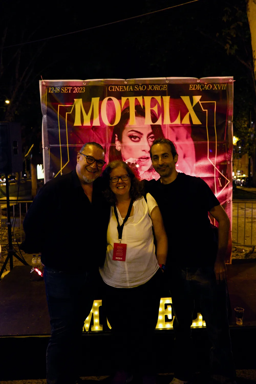 two men and a woman posing in front of a poster